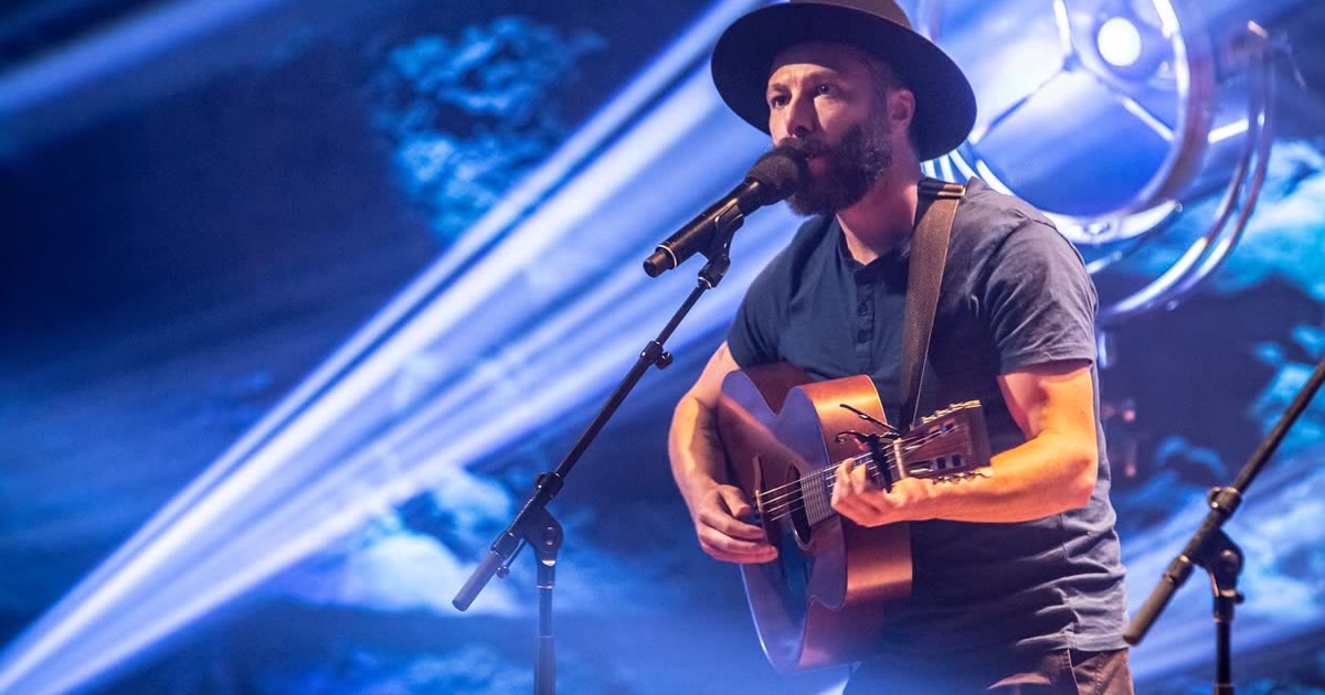 Singer-songwriter on stage in front of low blue beams, TV broadcast