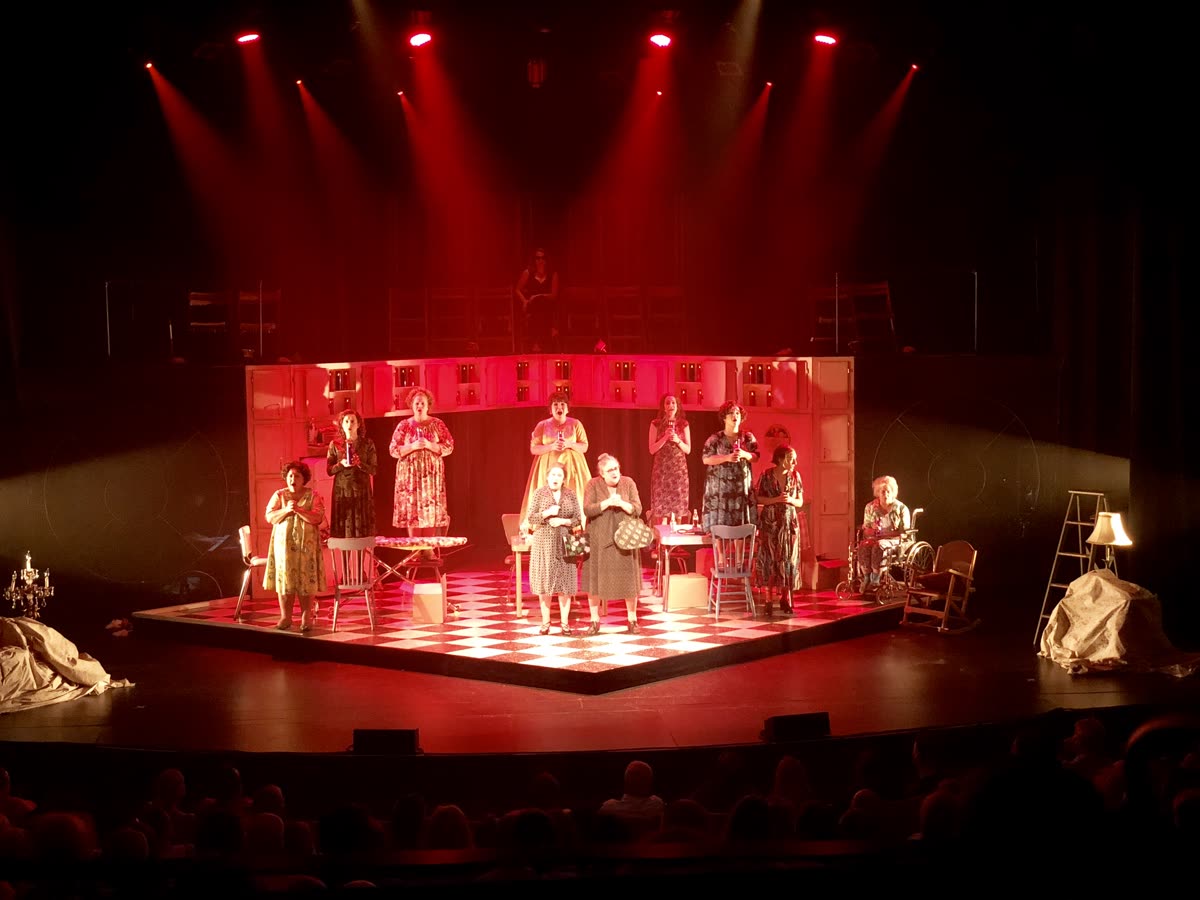 Scène de théâtre en lumière rouge, distribution au complet en scène