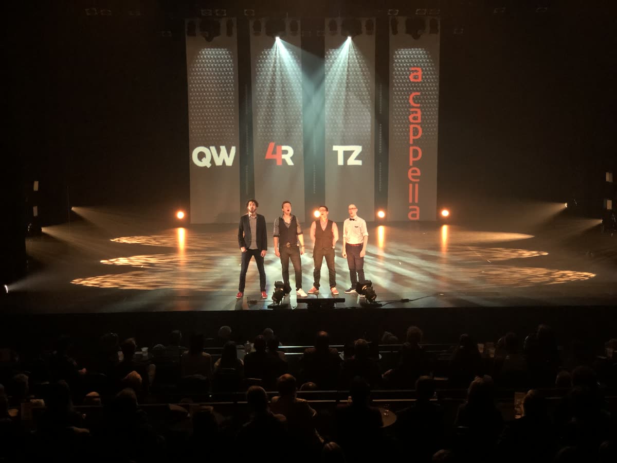 Quatuor a cappella en scène sous des faisceaux blancs, salle comble