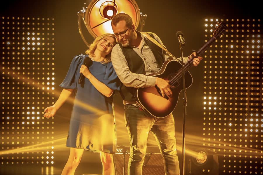 Duo en scène devant un mur de points lumineux dorés