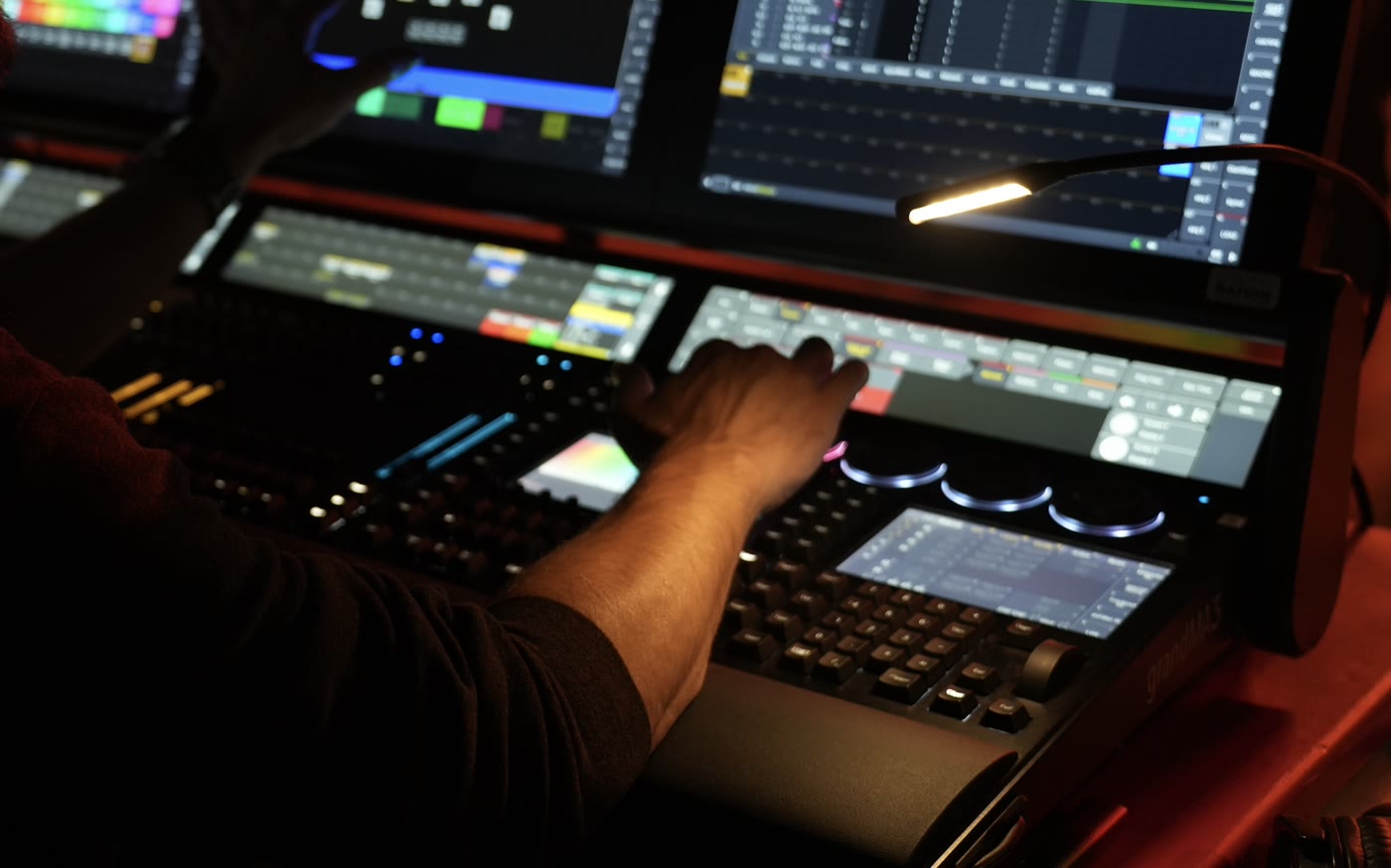 Hand on the faders of a grandMA console, programming screens lit